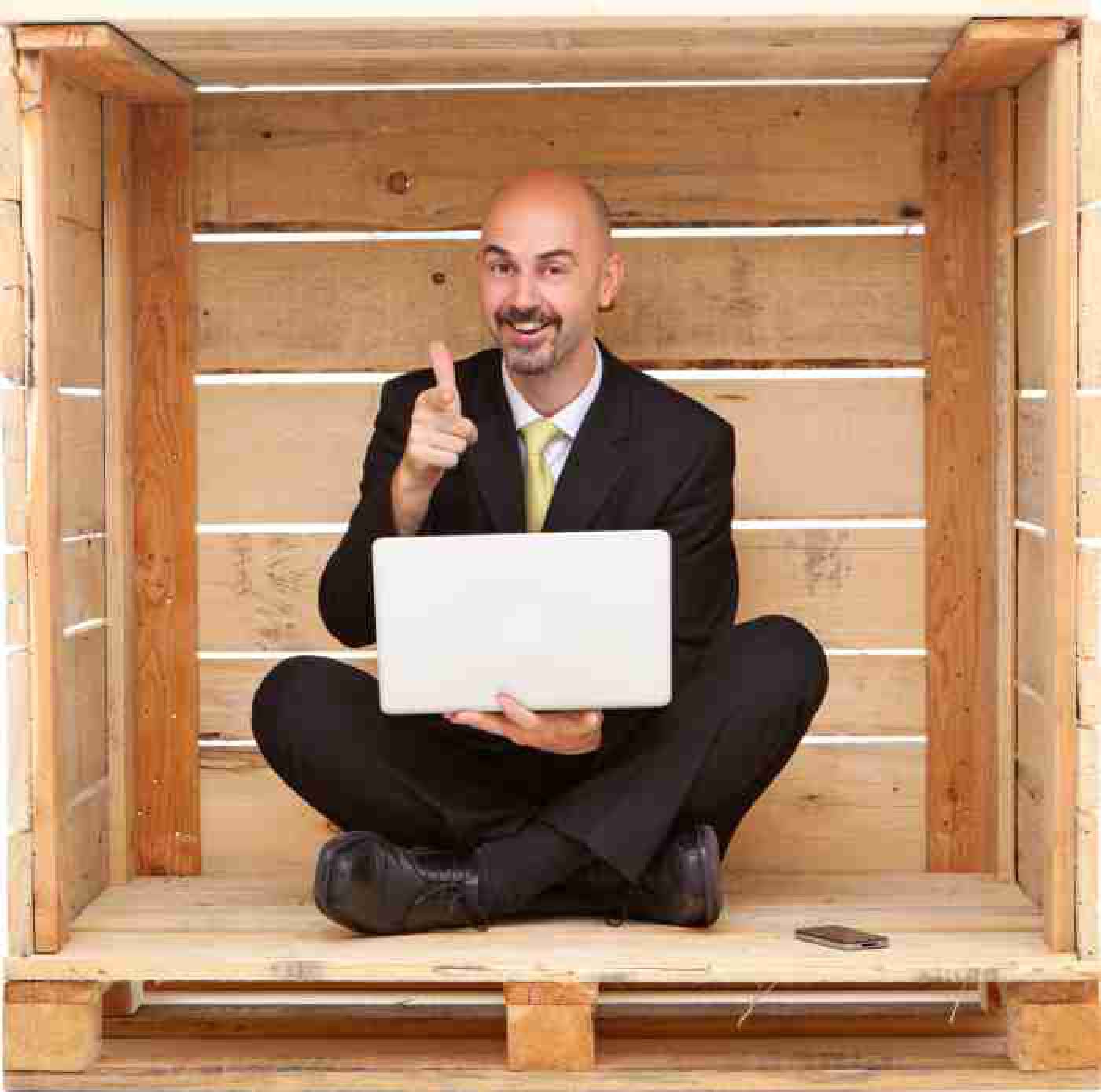 Smiling manager with laptop sitting inside wood box